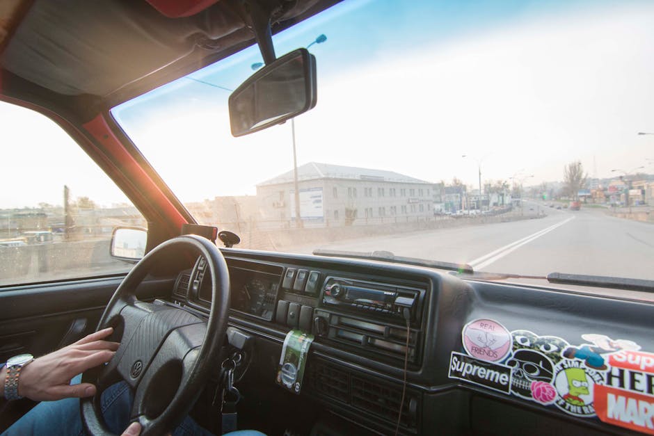 Interior view of a car dash with cityscape through windshield, sunny day.
