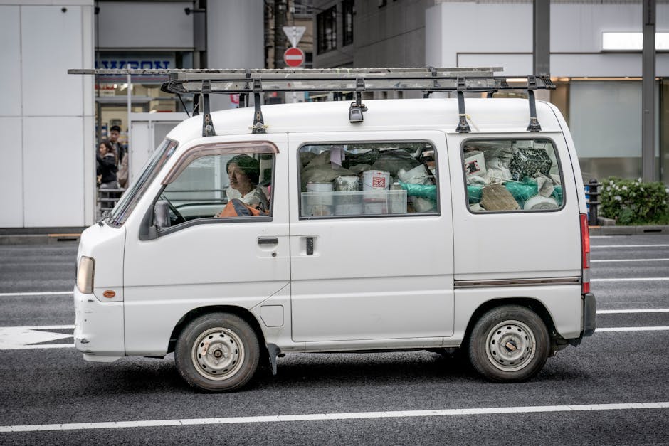 White utility van with cargo, parked on a Tokyo street, driver visible inside.