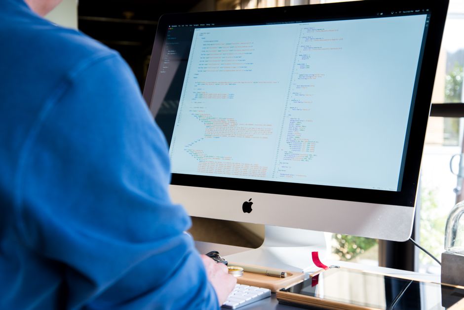 Programer u plavoj košulji kodira na iMacu